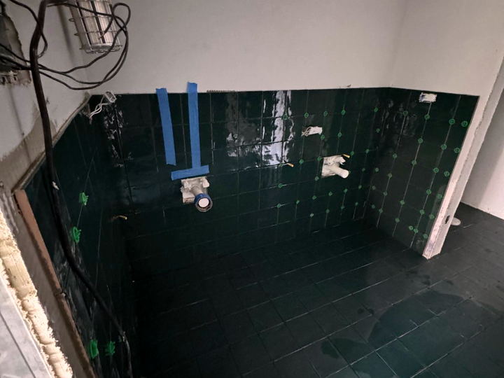 Dark green wall tile going up with spacers still in place, wiring exposed and a work light hanging