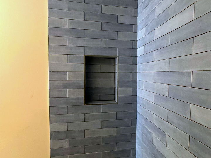 Shower wall in blue-grey subway tile with a recessed niche, photographed before the pan is tiled