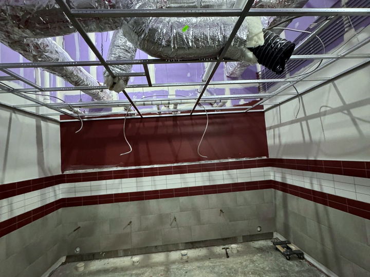 Ceiling grid and ductwork above a finished tile wainscot in a commercial space still under construction