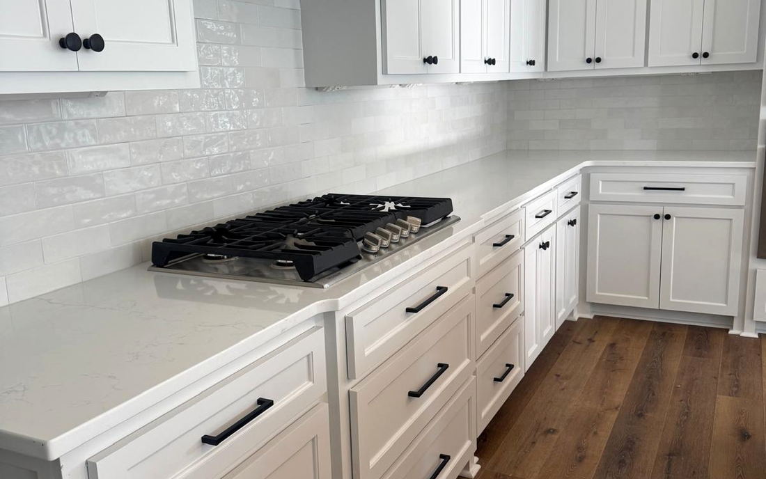 White kitchen run with subway backsplash carried around the corner, quartz counters and a wood plank floor