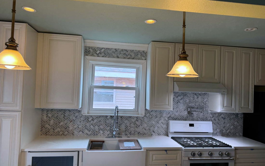Kitchen backsplash in marble herringbone mosaic running behind a farmhouse sink and up to the range hood