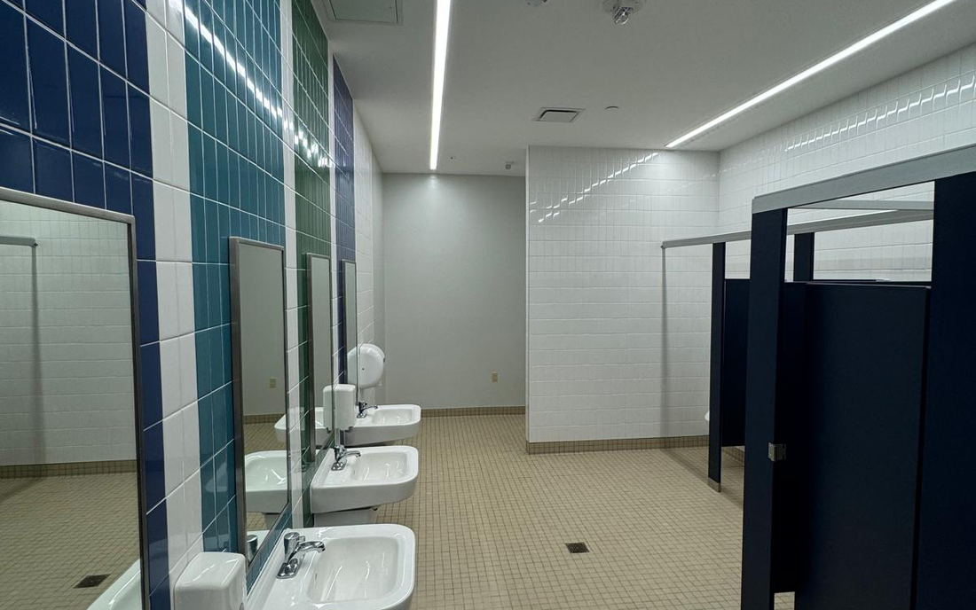 Commercial restroom with vertical bands of blue and green tile between white tile and a row of sinks with mirrors