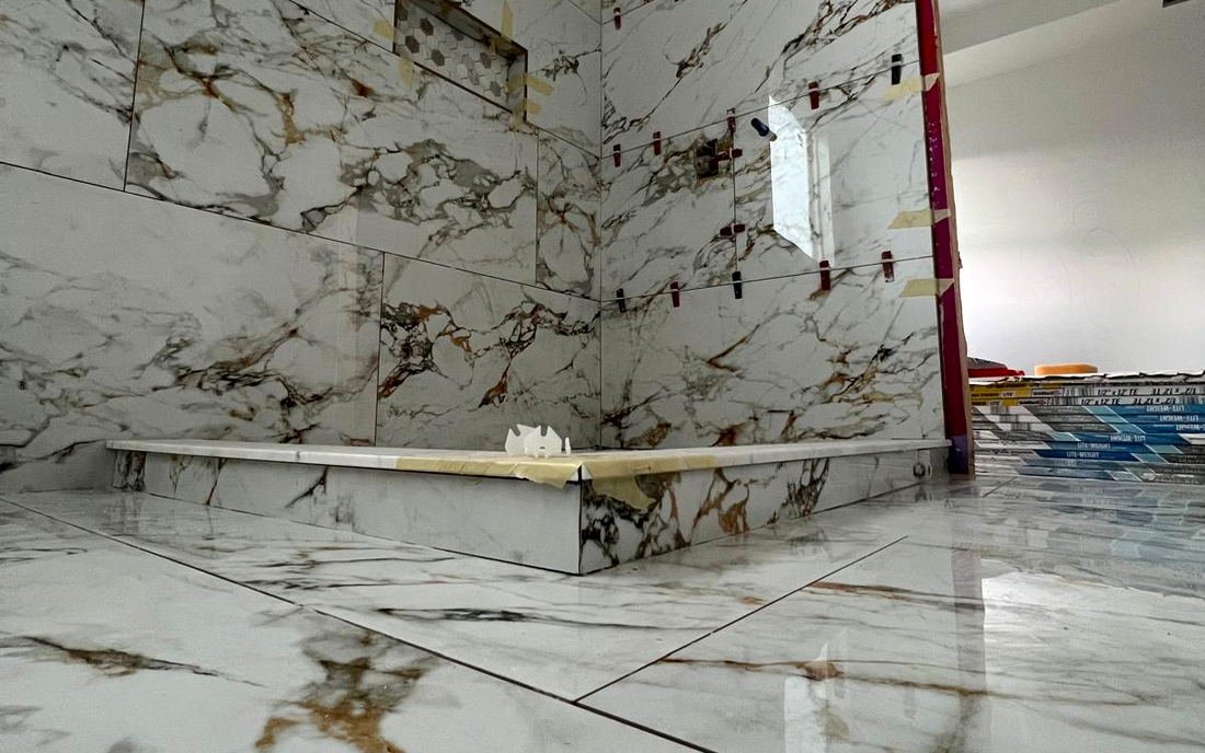 Low view of a Calacatta-look porcelain floor and shower curb with heavy gold and grey veining