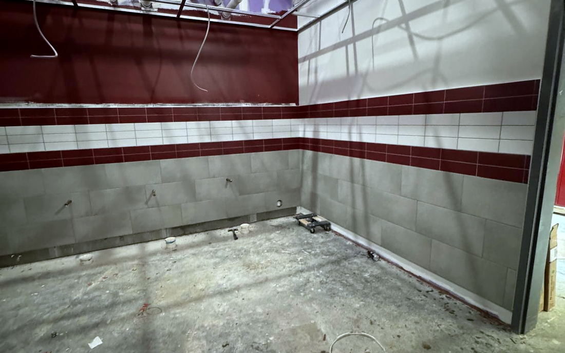 Commercial interior under construction with a tiled wainscot, a burgundy and white banding course and a bare concrete floor