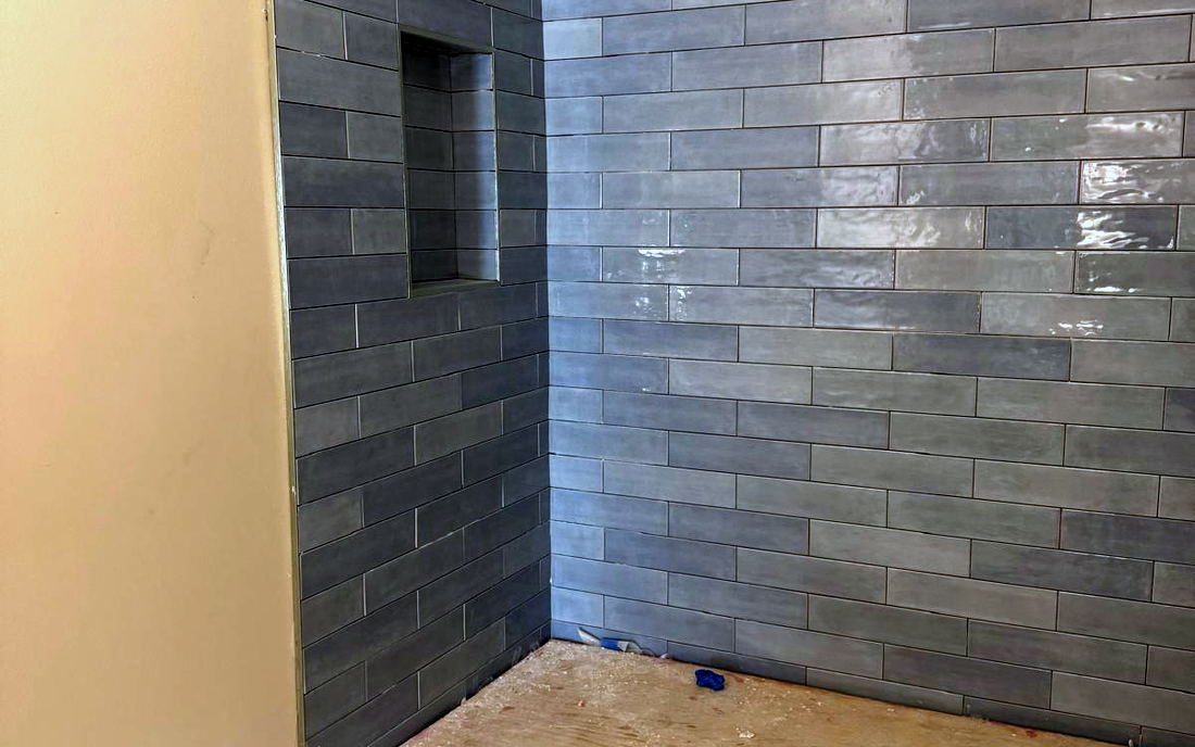 Blue-grey subway shower walls complete with the plywood pan base still exposed and waterproofing edge visible
