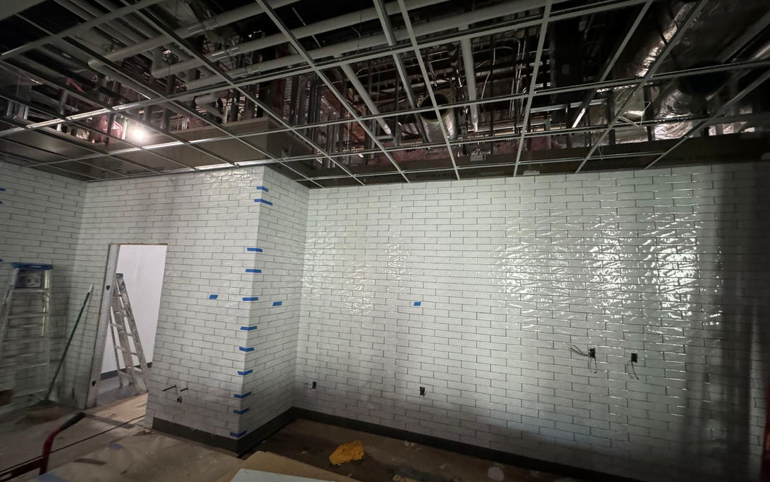 Commercial walls tiled in white subway with blue tape marking the corners, under an open ceiling grid