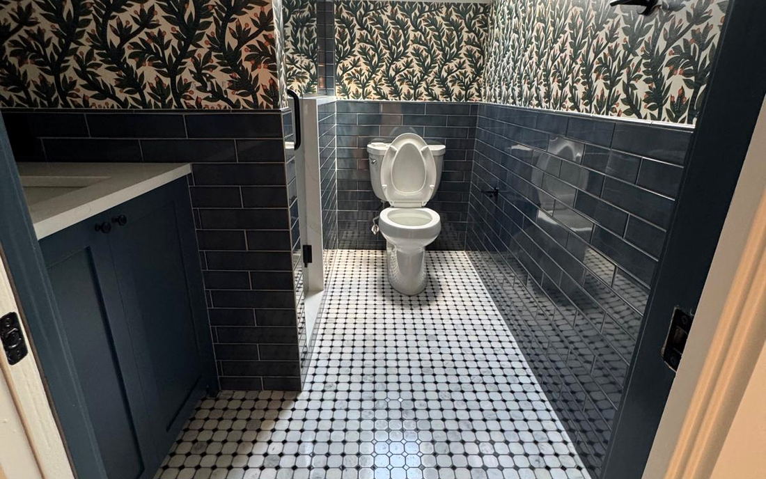 Bathroom with botanical wallpaper above a dark blue subway wainscot and a marble octagon-and-dot mosaic floor