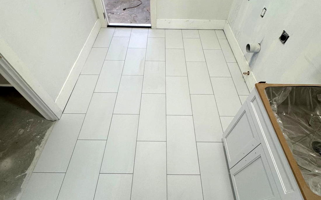 White floor tile installed in a narrow utility room, running lengthwise toward the doorway