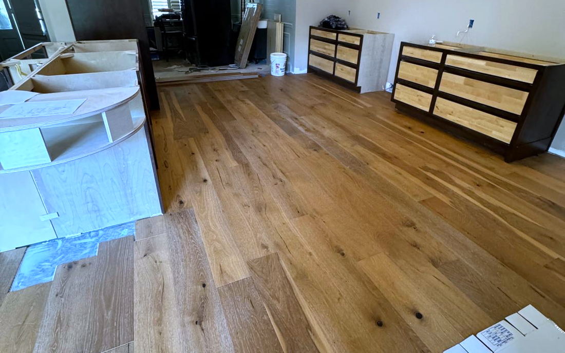 Wide-plank wire-brushed oak floor running through a living and dining area toward an arched window