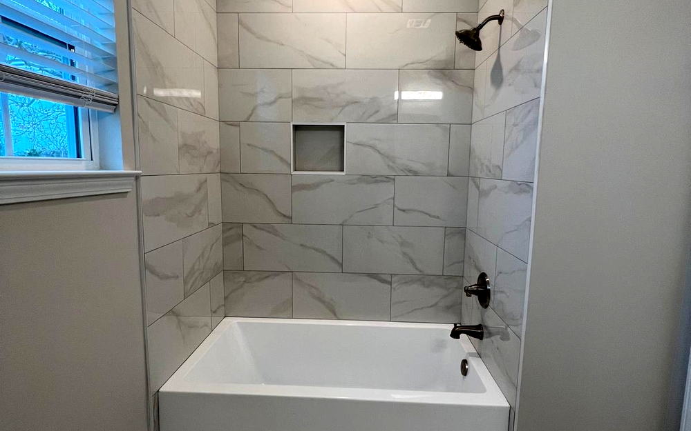 Tub surround in white marble-look porcelain with a recessed niche, a tiled ceiling line and a matching floor