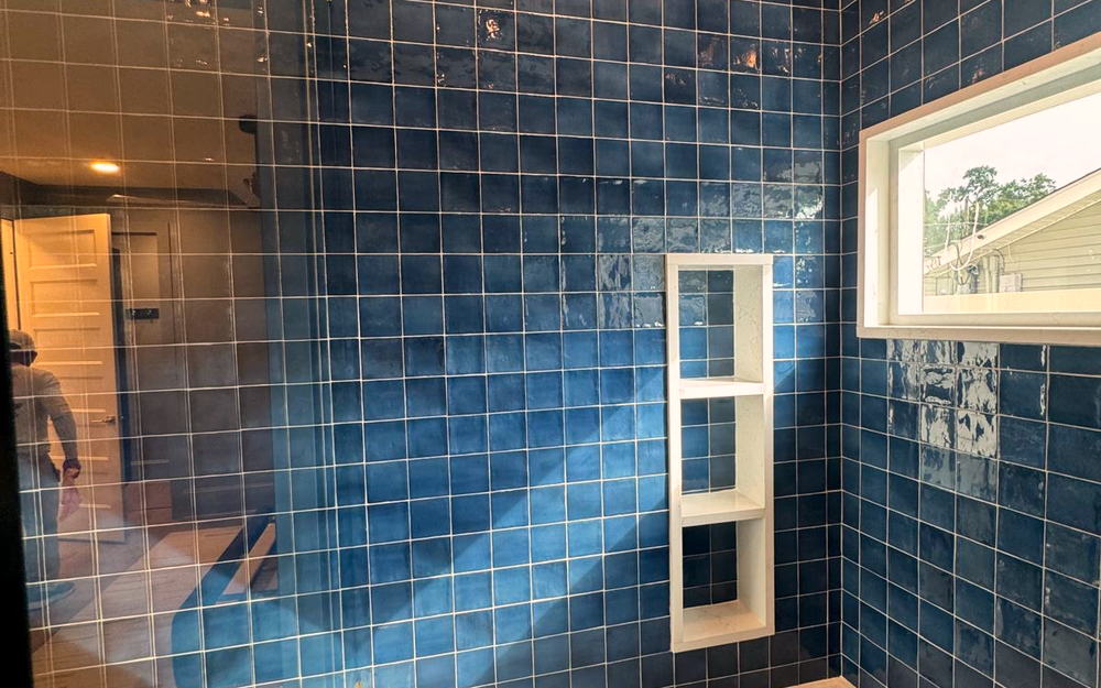 Detail of a navy glazed tile shower wall with a built-in quartz bench and a three-shelf recessed niche