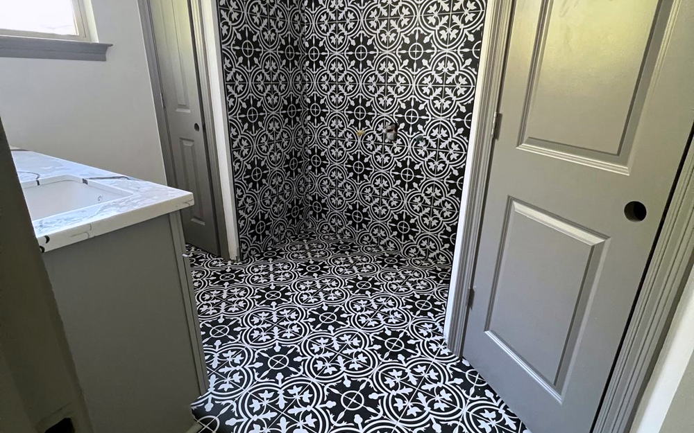 Shower and bathroom floor tiled in matching black and white patterned encaustic-look tile