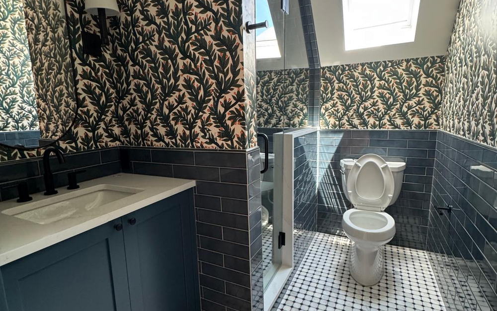 Bathroom with a navy vanity, quartz top, botanical wallpaper, blue subway wainscot and a marble mosaic floor