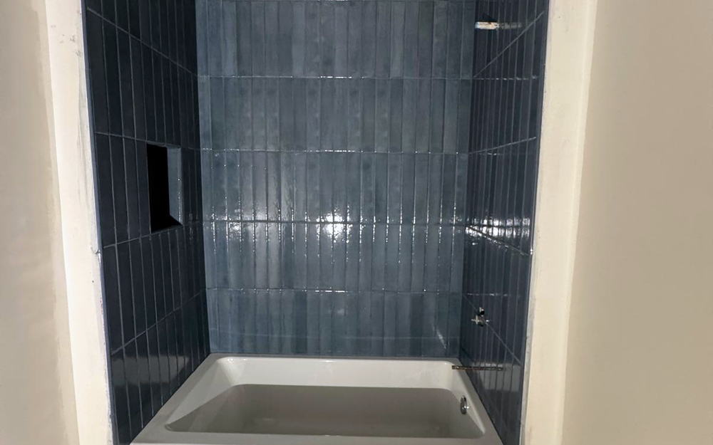 Tub surround in dark blue vertical stacked tile under a sloped ceiling, with the floor still unfinished