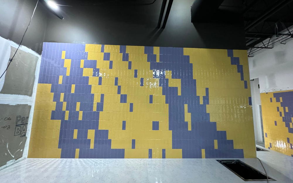 Yellow and purple pixelated tile wall behind a white quartz service counter in a commercial fit-out