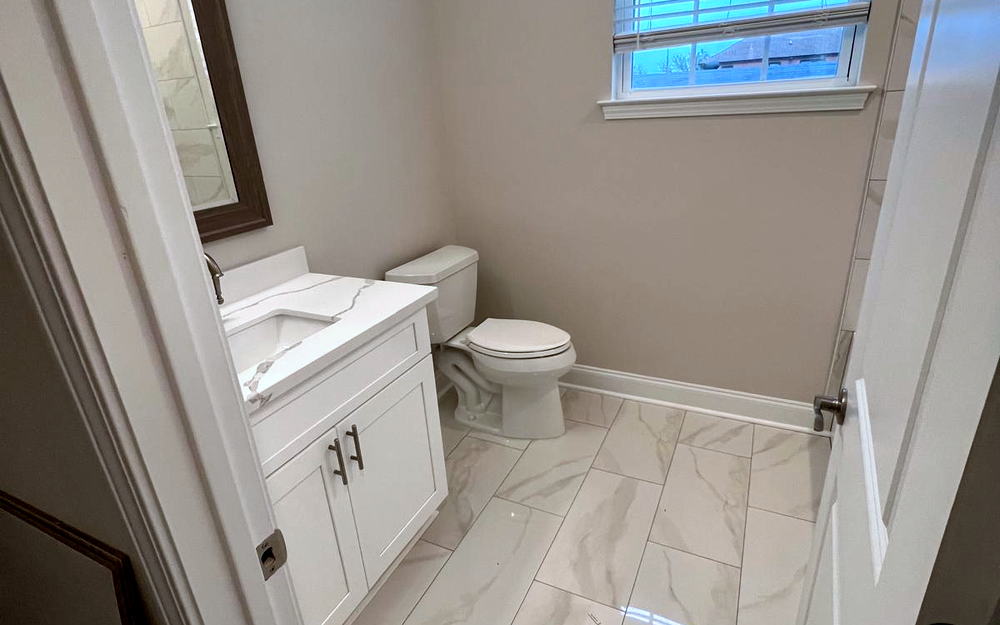 Small finished bathroom with a marble-look porcelain floor, white vanity with quartz top and a framed mirror