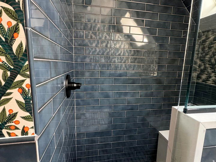 Close view of a dark blue subway tiled shower wall with a matte black valve and the sloped ceiling above