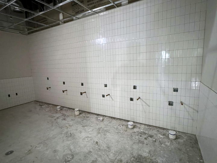 Utility room tiled in small white square tile with plumbing stub-outs and electrical boxes left exposed on a concrete floor