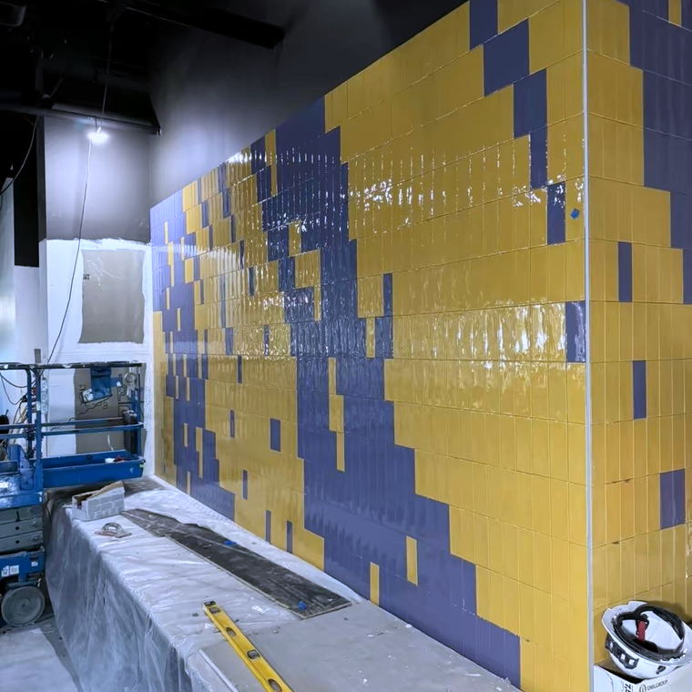 Yellow and purple pixelated tile wall photographed along its length with a lift and levels in the foreground