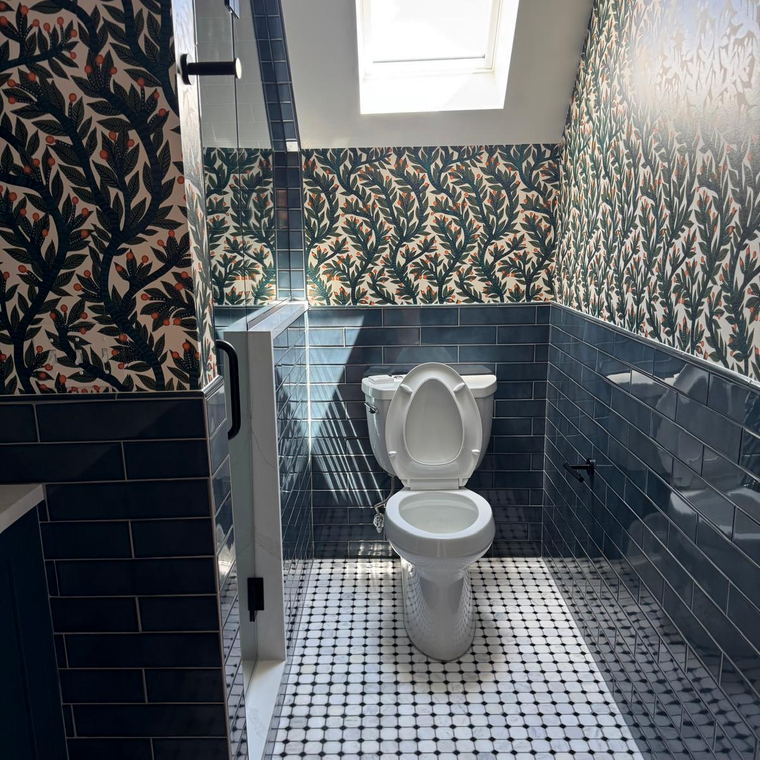 Bathroom under a skylight with botanical wallpaper, blue subway wainscot and a marble octagon-and-dot floor