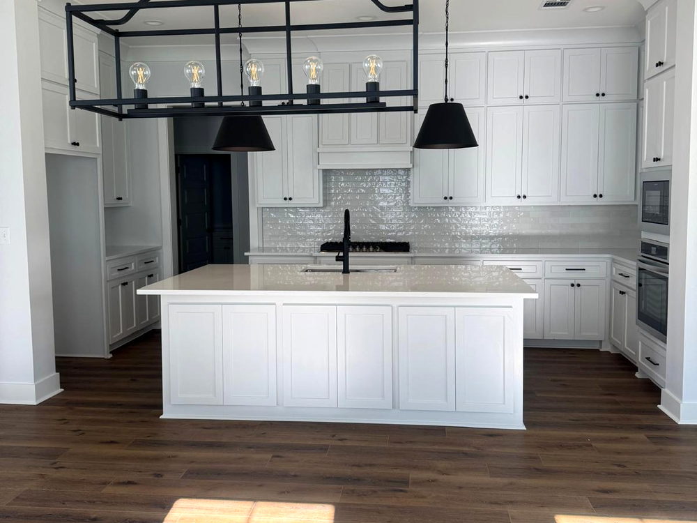 Open white kitchen with an island, black pendant lights, subway backsplash and a wide-plank wood floor