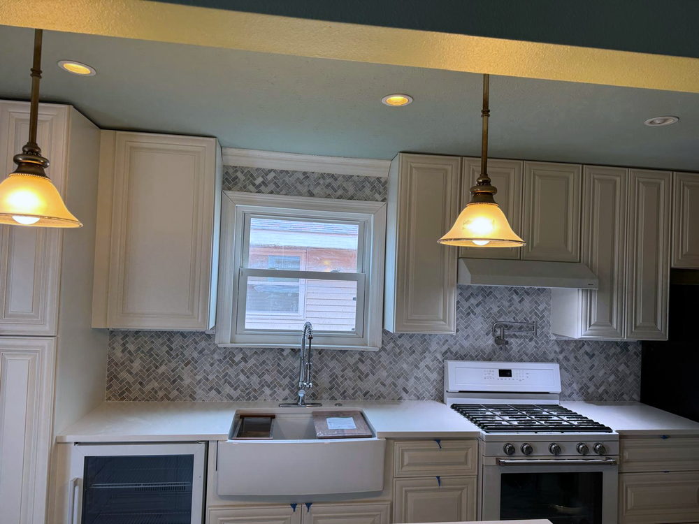 Kitchen backsplash in marble herringbone mosaic running behind a farmhouse sink and up to the range hood