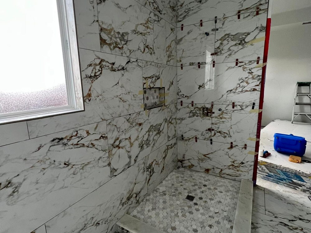 Shower walls in Calacatta-look porcelain with leveling clips and tape still in place during installation