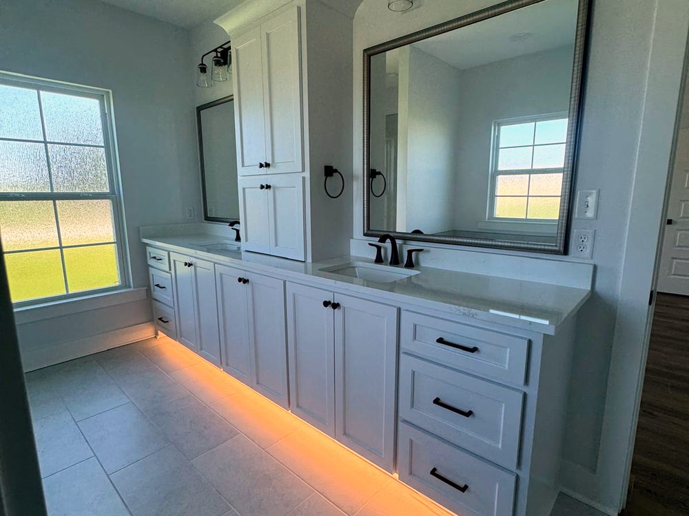 Double vanity with quartz tops, framed mirrors and under-cabinet lighting above a porcelain tile floor