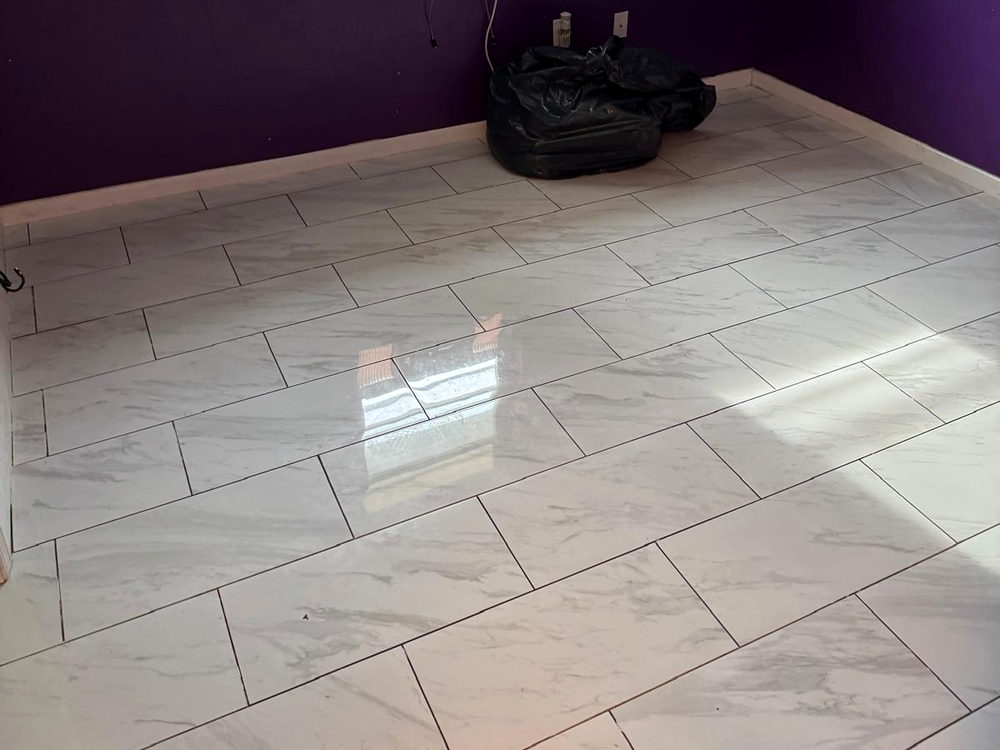 Large-format marble-look porcelain floor tile installed in a staggered layout across a bedroom