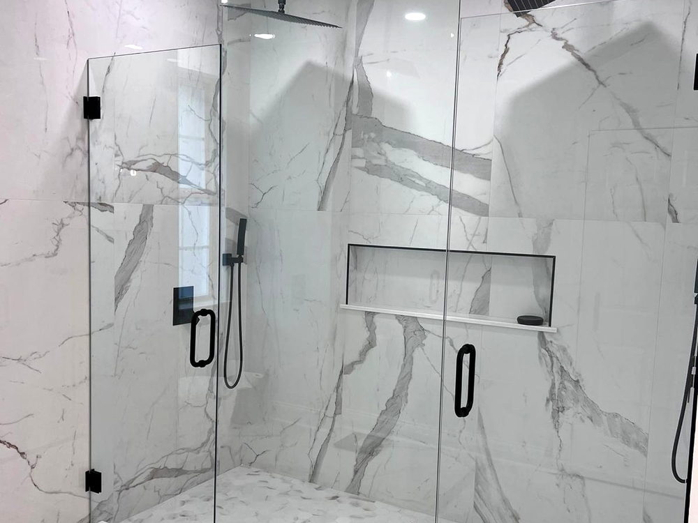 Walk-in shower lined in large-format marble-look porcelain with two rain heads, a recessed shelf and frameless glass