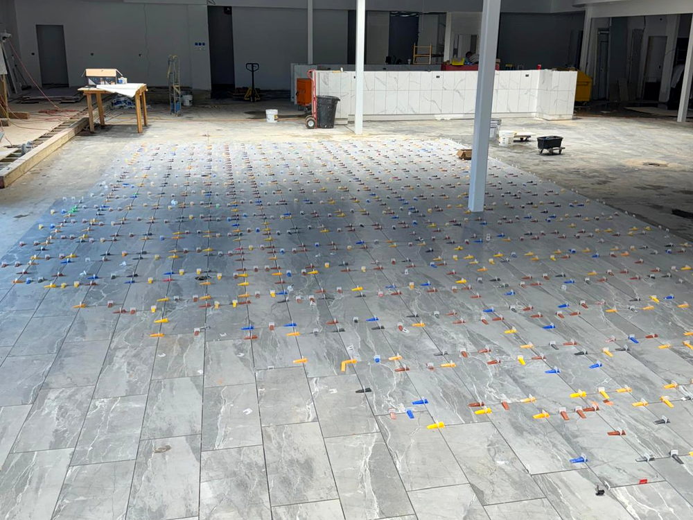 Large commercial floor being installed in grey marble-look porcelain with leveling wedges across the whole field