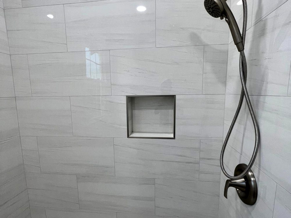 Shower lined in grey striated porcelain with a recessed niche and a natural pebble mosaic pan