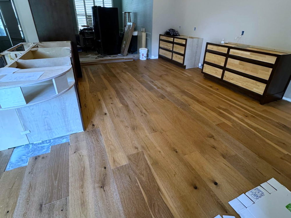 Wide-plank floor installed through a living and dining area, with boxes and protective boards still on site