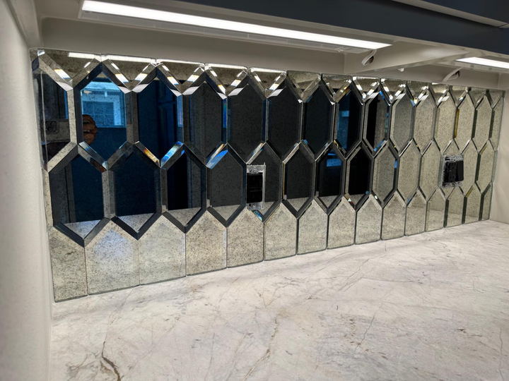 Antique mirrored hexagon backsplash with beveled edges seen at an angle under cabinet lighting