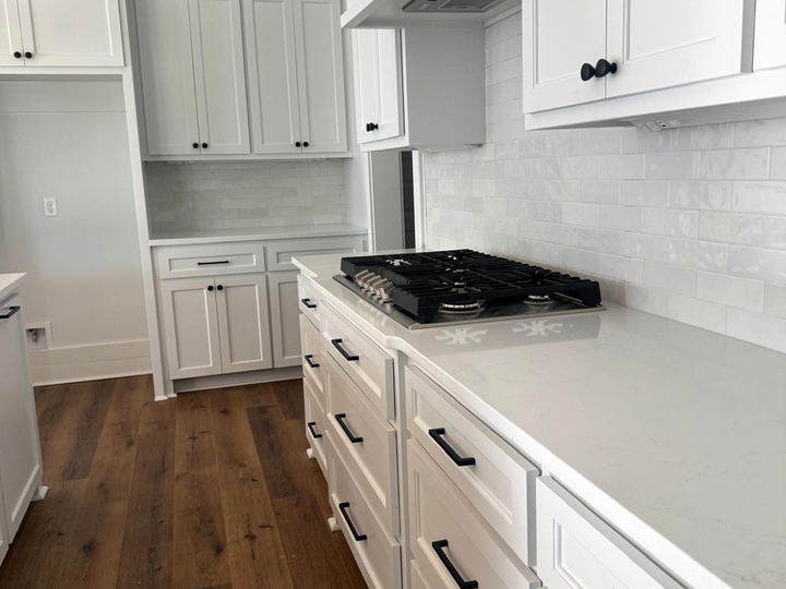 White kitchen with a handmade-look white subway backsplash behind a gas cooktop, quartz counters and a wood-look floor