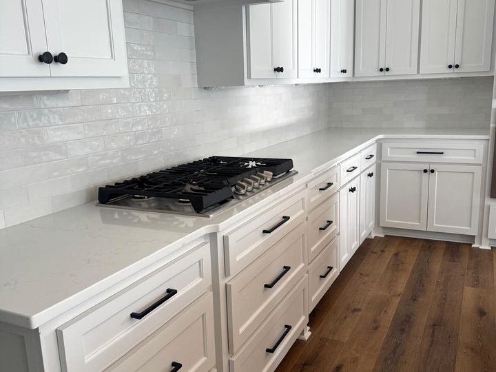 White kitchen run with subway backsplash carried around the corner, quartz counters and a wood plank floor