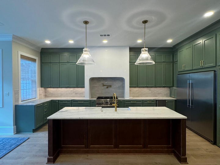 Kitchen with deep green cabinets, a dark wood island under a marble top, a light tile backsplash and a wide-plank floor