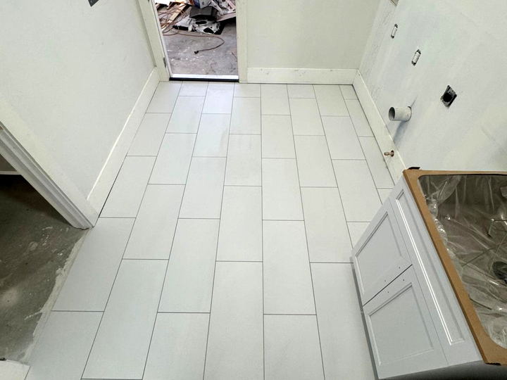 White floor tile installed in a narrow utility room, running lengthwise toward the doorway