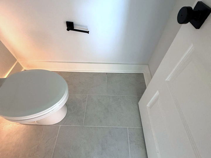 Small bathroom with a grey porcelain tile floor running under the door and a white baseboard