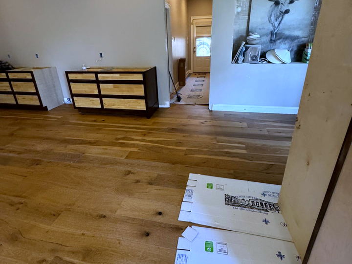 Wide-plank oak floor installed through a bedroom with furniture staged along the wall and protective boards down