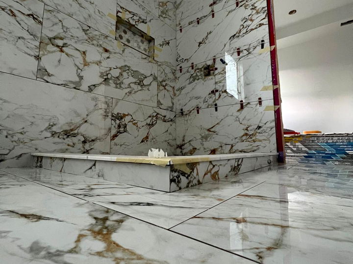Low view of a Calacatta-look porcelain floor and shower curb with heavy gold and grey veining