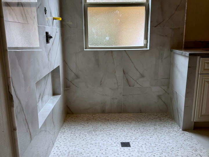 Walk-in shower in Calacatta-look porcelain with a window, a long recessed shelf and a small square mosaic pan
