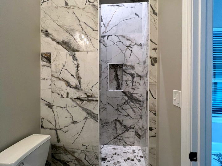 Tall recessed shower niche in white and grey marble-look porcelain with a hexagon mosaic base, next to a toilet