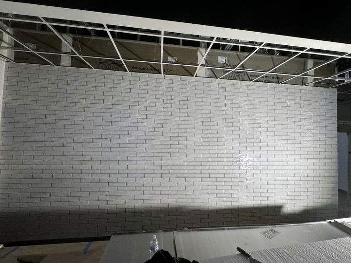 Long wall of white subway tile in a commercial space with a dark base course and ceiling grid above