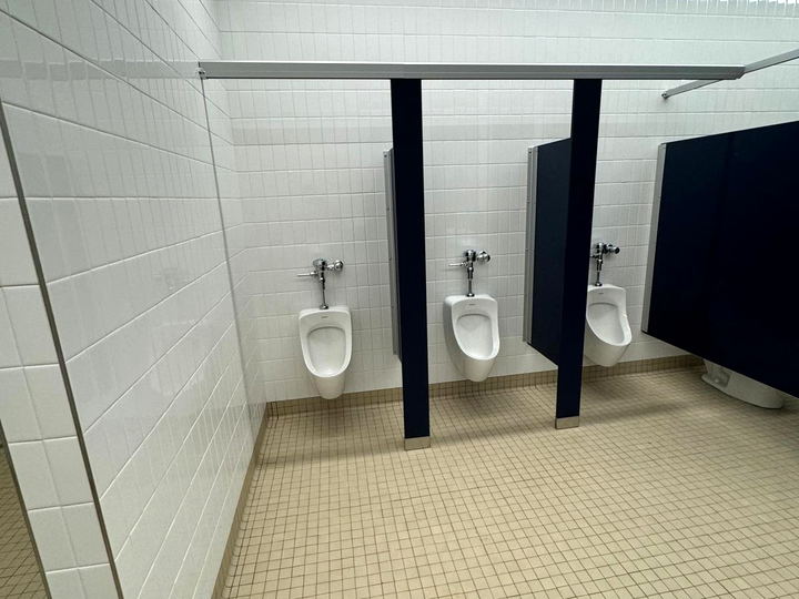 Commercial restroom with white square wall tile, a tiled floor and three urinals between privacy screens