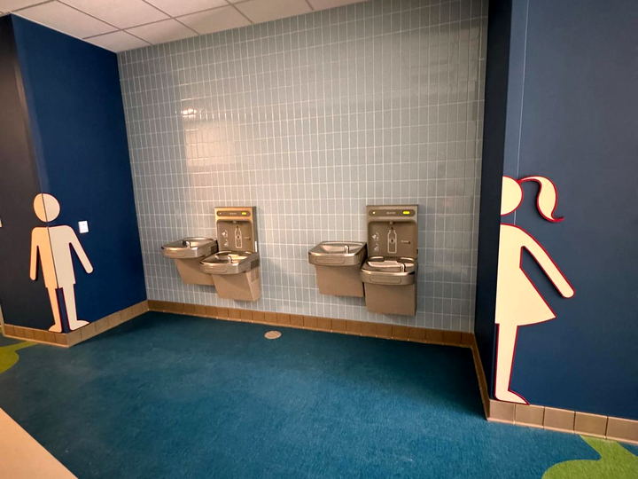 Drinking fountain alcove with a pale blue tile wall between two navy walls in a school corridor