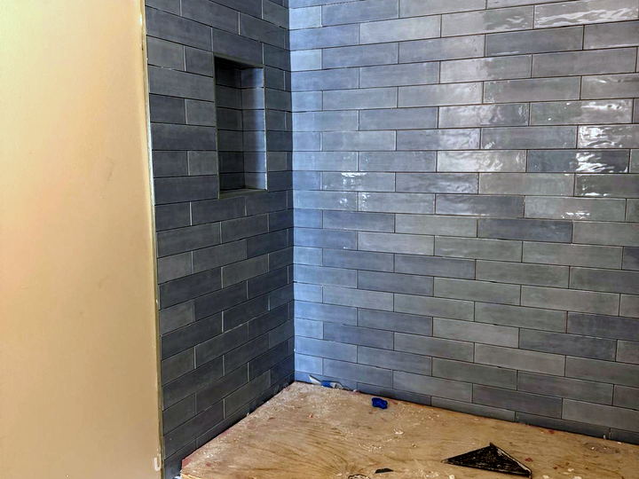Blue-grey subway shower walls complete with the plywood pan base still exposed and waterproofing edge visible