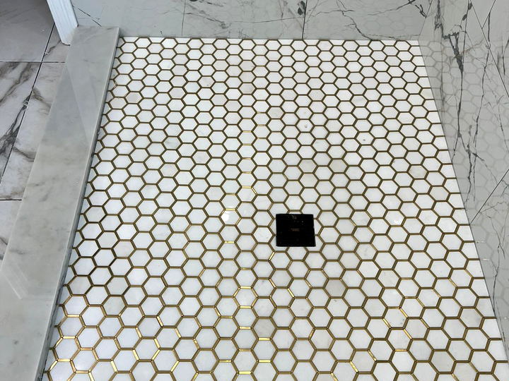 Shower pan in white marble hexagon mosaic with gold-toned grout and a marble curb