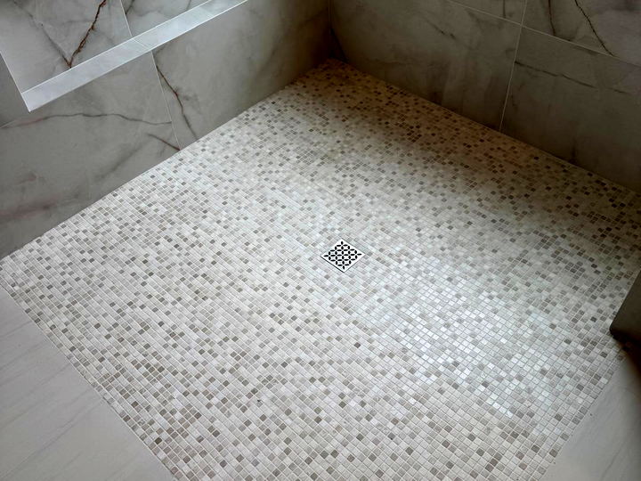 Overhead view of a shower pan in fine square marble mosaic with a decorative drain and a diagonal border