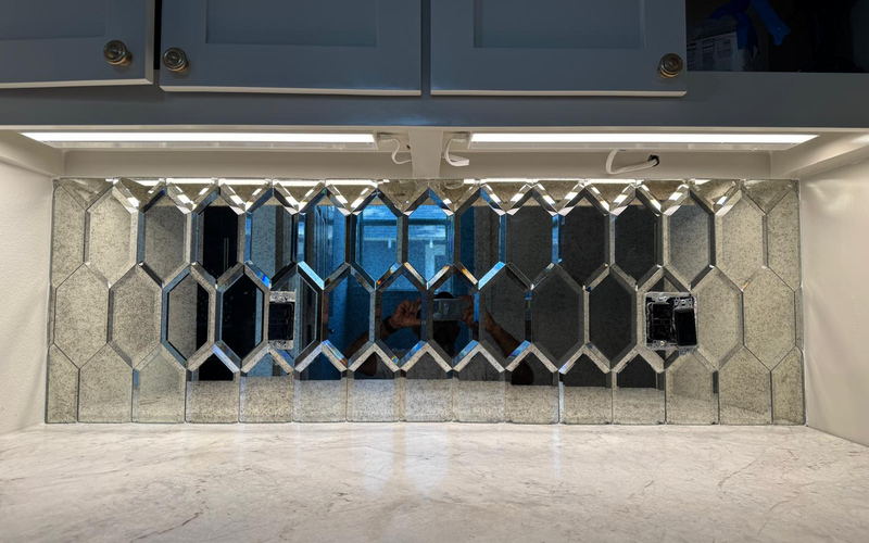 Antique mirrored hexagon backsplash centered between wall cabinets above a marble countertop